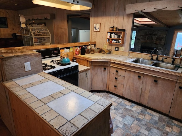 kitchen with gas stove, sink, tile countertops, and wooden walls