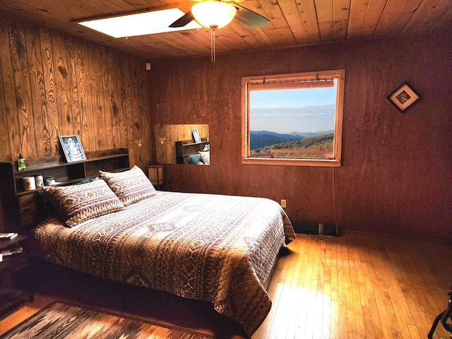 bedroom featuring light wood-type flooring, wooden ceiling, ceiling fan, and wood walls