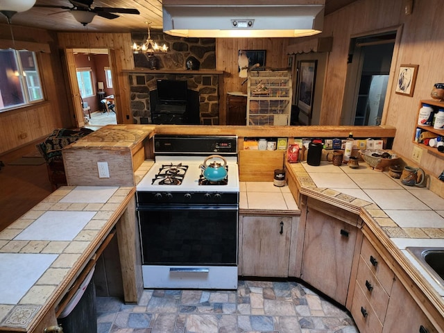 kitchen featuring ceiling fan with notable chandelier, white gas range, tile countertops, and wooden walls