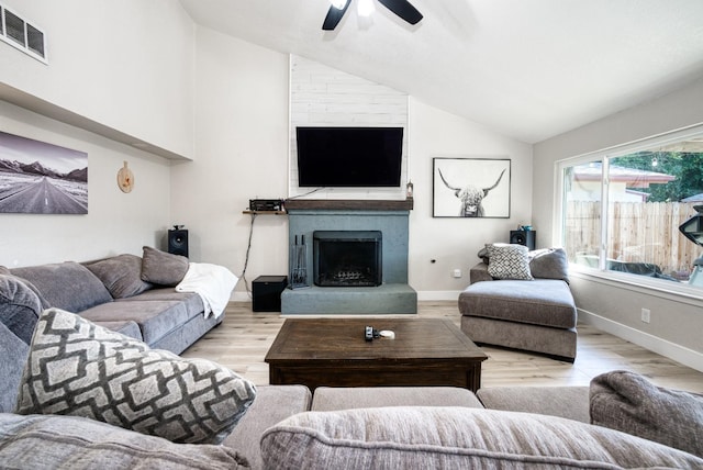 living room featuring lofted ceiling, a large fireplace, ceiling fan, and light wood-type flooring