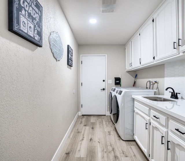 laundry area with cabinets, washing machine and dryer, sink, and light hardwood / wood-style floors