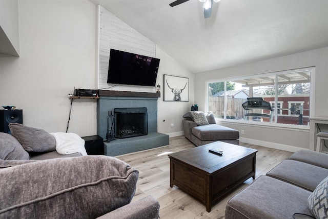 living room featuring ceiling fan, a fireplace, vaulted ceiling, and light wood-type flooring