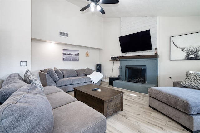 living room featuring ceiling fan, a fireplace, high vaulted ceiling, and light wood-type flooring