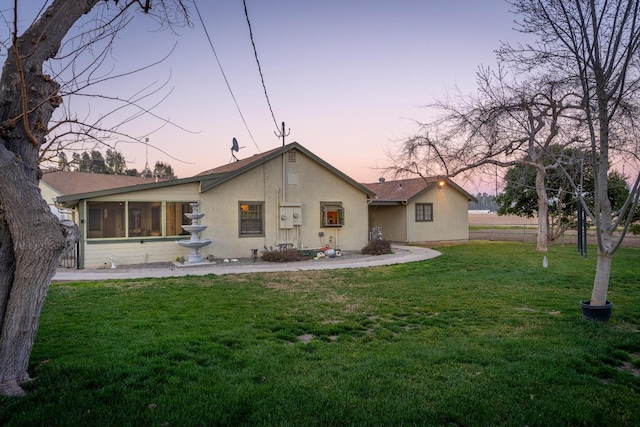 back house at dusk featuring a sunroom and a lawn