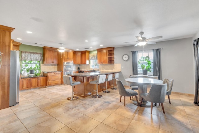 kitchen with light tile patterned flooring, backsplash, a kitchen breakfast bar, ceiling fan, and stainless steel appliances