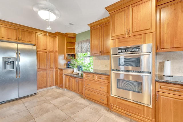 kitchen featuring dark stone countertops, backsplash, light tile patterned floors, and stainless steel appliances