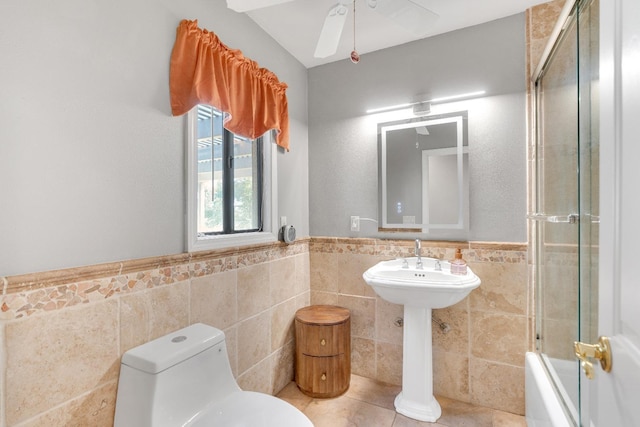 bathroom featuring tile patterned floors, toilet, combined bath / shower with glass door, tile walls, and ceiling fan