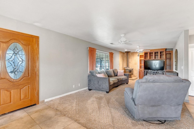 tiled living room featuring a wood stove and ceiling fan