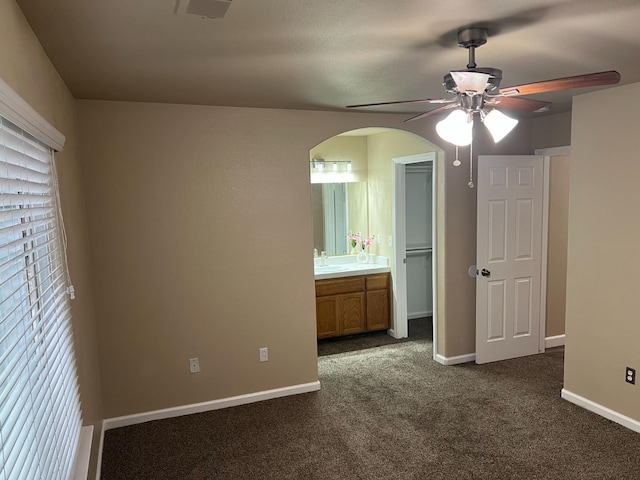 unfurnished bedroom with arched walkways, connected bathroom, a sink, baseboards, and dark carpet