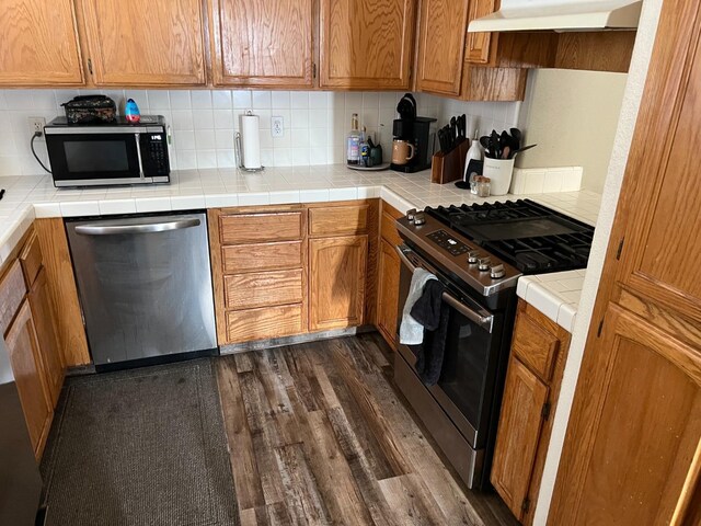 kitchen with tasteful backsplash, tile countertops, stainless steel appliances, and dark hardwood / wood-style floors