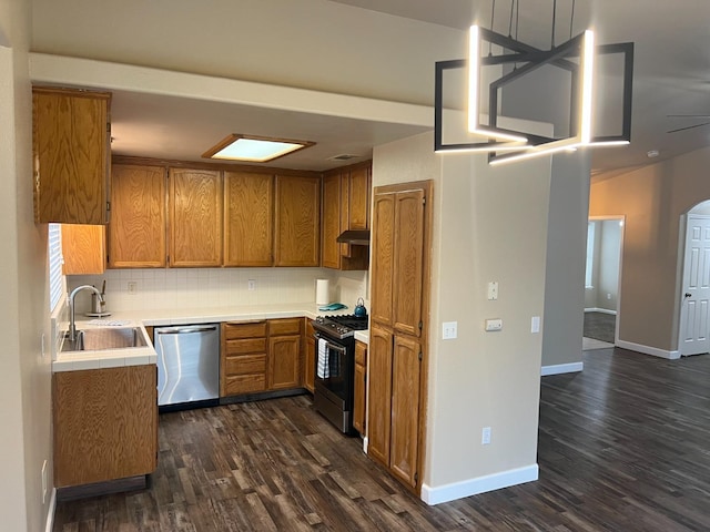 kitchen featuring brown cabinetry, tile countertops, appliances with stainless steel finishes, under cabinet range hood, and a sink