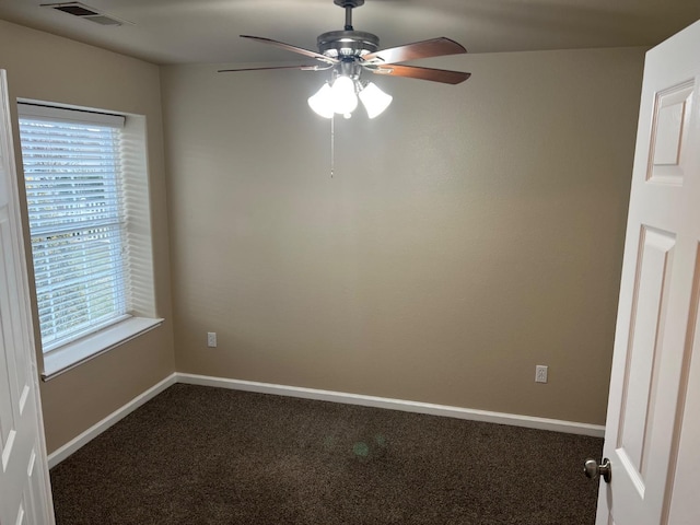 unfurnished room featuring a healthy amount of sunlight, visible vents, dark carpet, and baseboards