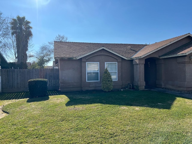 view of side of property with stucco siding, fence, a lawn, and roof with shingles