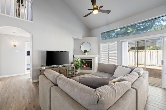 living room with ceiling fan, high vaulted ceiling, and light wood-type flooring