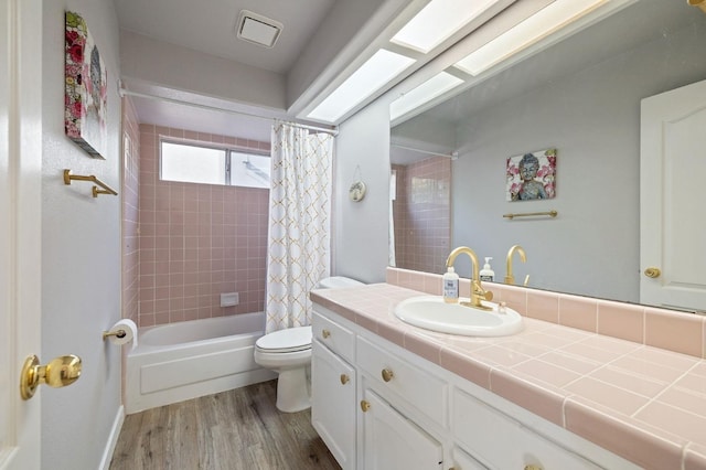 full bathroom with toilet, wood-type flooring, a skylight, vanity, and shower / bathtub combination with curtain