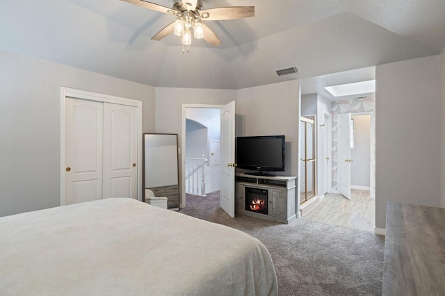 bedroom featuring lofted ceiling with skylight, light carpet, ceiling fan, and a closet