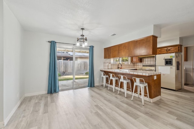 kitchen with range, decorative light fixtures, light wood-type flooring, white refrigerator, and kitchen peninsula