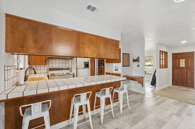 kitchen with range with two ovens, sink, tile counters, and kitchen peninsula