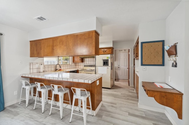 kitchen with sink, white appliances, tile counters, kitchen peninsula, and light wood-type flooring