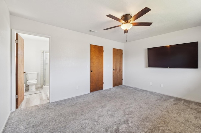 unfurnished bedroom with light carpet, ensuite bath, ceiling fan, and two closets