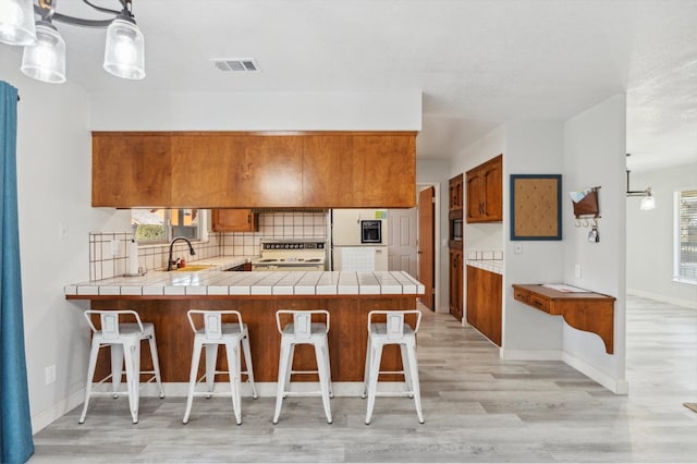 kitchen featuring kitchen peninsula, sink, hanging light fixtures, and stove