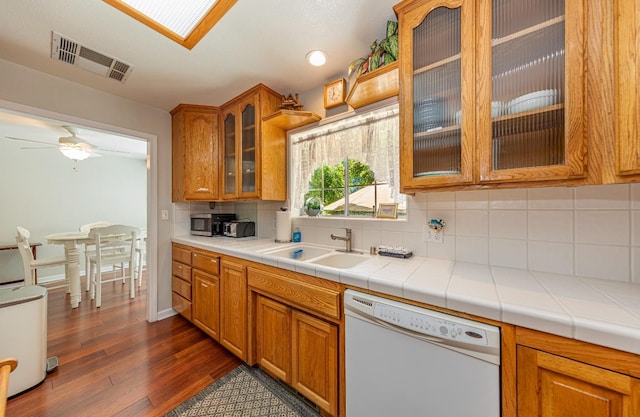 kitchen with visible vents, decorative backsplash, dishwasher, dark wood-style floors, and a sink