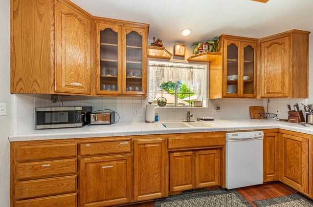 kitchen with decorative backsplash, stainless steel microwave, dark wood-type flooring, white dishwasher, and a sink