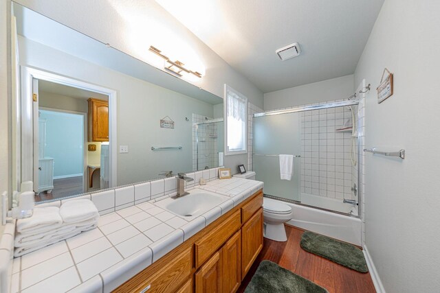 bathroom with baseboards, toilet, wood finished floors, combined bath / shower with glass door, and vanity