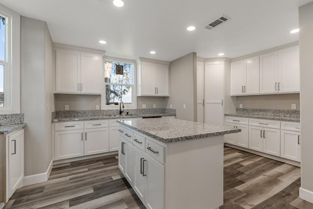 kitchen with white cabinetry, dark hardwood / wood-style flooring, light stone counters, and a kitchen island