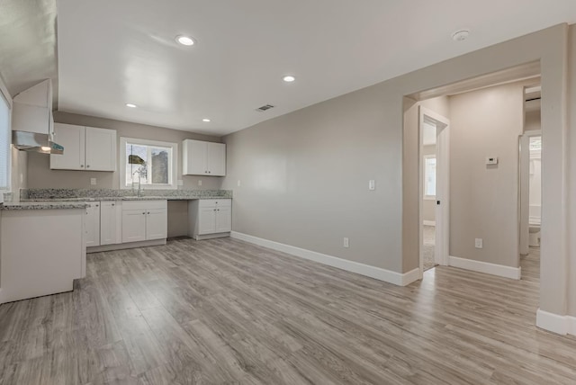 kitchen with sink, light stone countertops, white cabinets, and light wood-type flooring