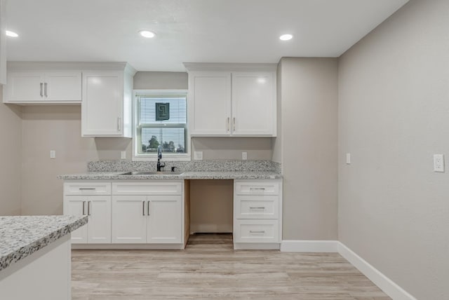 kitchen with white cabinetry, sink, and light stone counters