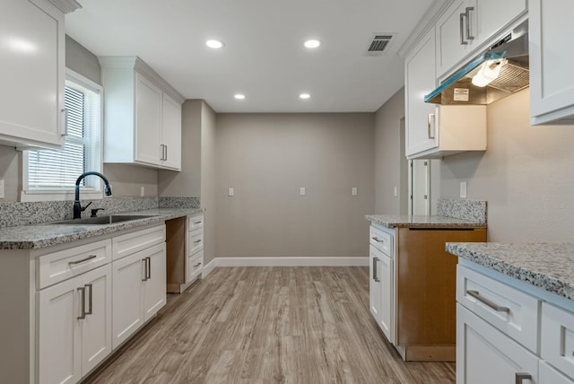 kitchen with white cabinetry, light stone countertops, sink, and light hardwood / wood-style floors