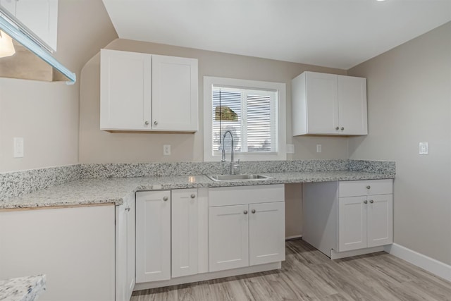 kitchen with white cabinetry, light stone countertops, sink, and light hardwood / wood-style floors