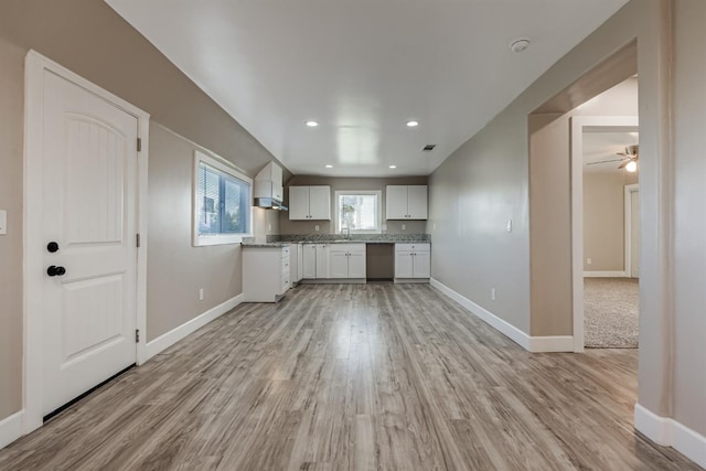 kitchen featuring sink, wall chimney range hood, white cabinets, and light hardwood / wood-style floors