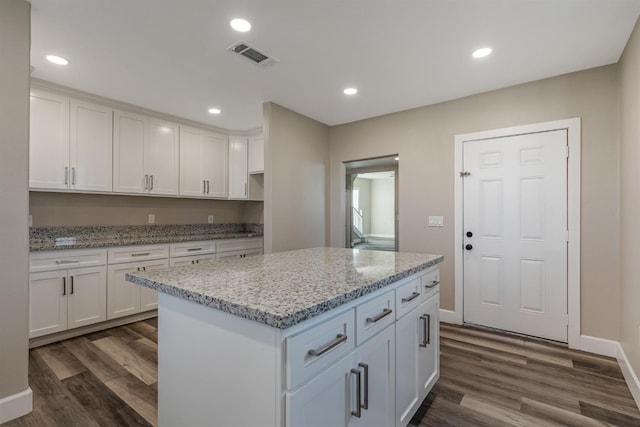 kitchen featuring dark hardwood / wood-style flooring, light stone countertops, white cabinets, and a kitchen island