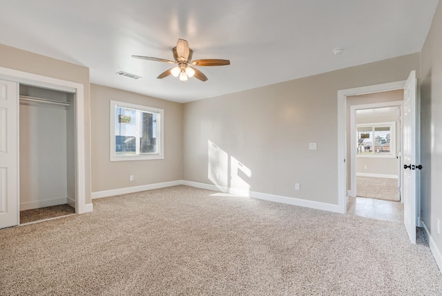 unfurnished bedroom with multiple windows, light colored carpet, ceiling fan, and a closet