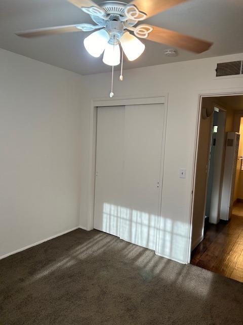 unfurnished bedroom with dark colored carpet, a closet, visible vents, and a ceiling fan