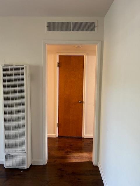 corridor with dark wood-style flooring, a heating unit, visible vents, and baseboards