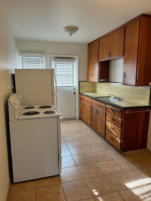 kitchen with white appliances, tasteful backsplash, tile counters, brown cabinetry, and a sink