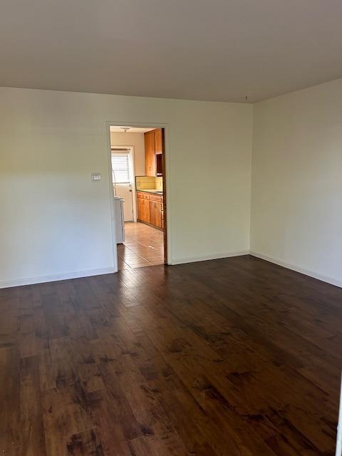 empty room with dark wood-type flooring and baseboards