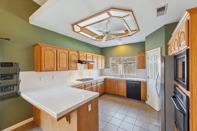 kitchen with light tile patterned flooring, kitchen peninsula, tasteful backsplash, tile counters, and black appliances