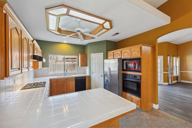 kitchen with black appliances, sink, tile counters, light tile patterned floors, and kitchen peninsula