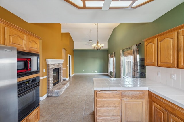 kitchen with vaulted ceiling, pendant lighting, tile countertops, black oven, and stainless steel fridge