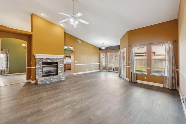 unfurnished living room with a brick fireplace, wood-type flooring, high vaulted ceiling, and ceiling fan