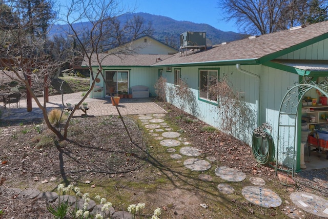 back of house with central air condition unit, a mountain view, a shingled roof, and a patio