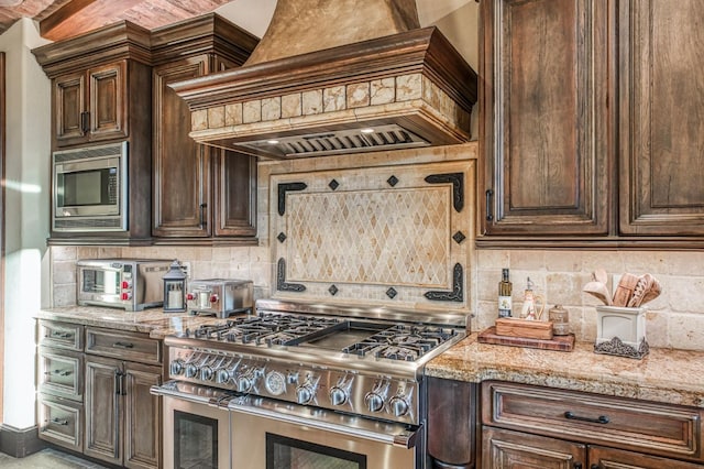 kitchen with appliances with stainless steel finishes, custom range hood, light stone counters, and decorative backsplash