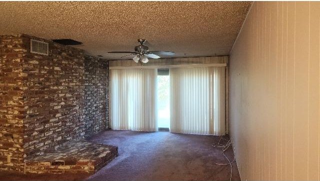 unfurnished room featuring ceiling fan, dark carpet, wooden walls, and a textured ceiling