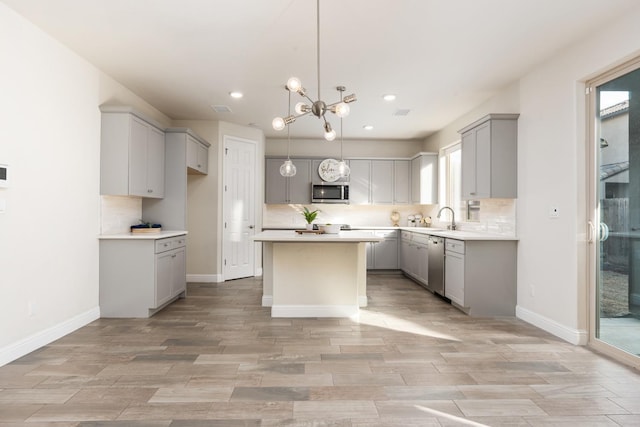 kitchen with gray cabinetry, an inviting chandelier, decorative light fixtures, appliances with stainless steel finishes, and a kitchen island