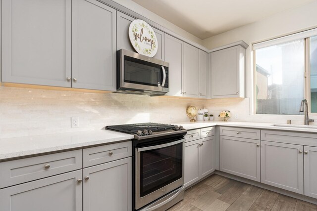 kitchen with appliances with stainless steel finishes, sink, gray cabinetry, decorative backsplash, and light stone counters