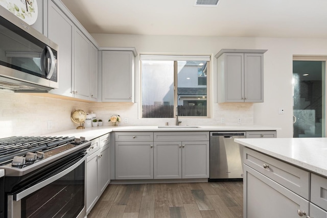 kitchen with sink, tasteful backsplash, wood-type flooring, gray cabinets, and stainless steel appliances